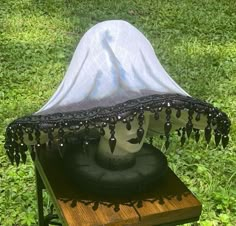 a white cloth covered hat sitting on top of a wooden box in the grass with beads hanging from it's sides