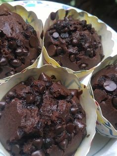 four chocolate muffins sitting in paper cups on a plate