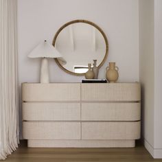 a white dresser topped with a mirror and vases next to a lamp on top of a hard wood floor