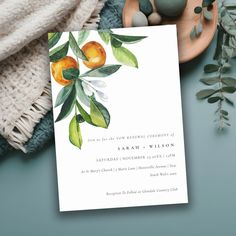 a wedding card with oranges and leaves on it next to some rocks, greenery