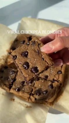 a hand is picking up a chocolate chip cookie from a wrapper on top of parchment paper