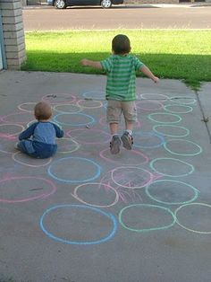 two young boys playing with colored chalk circles on the sidewalk in front of a house