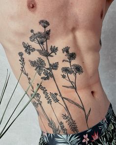 a man's back with flowers and leaves tattooed on his lower half, while he is wearing swim trunks