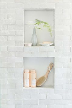 a white brick wall with two shelves holding various items and a vase on the shelf