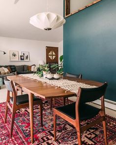 a dining room table and chairs in front of a blue wall with plants on it