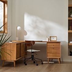 a desk with a chair, clock and potted plant in front of the window