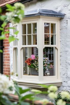 a window that has some flowers in the pot on it's sill next to a brick building