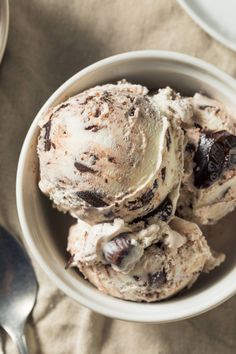 three scoops of ice cream in a white bowl on a table with spoons