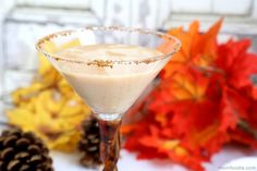 a drink in a martini glass next to autumn leaves