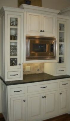 a kitchen with white cabinets and black counter tops in front of a silver microwave oven