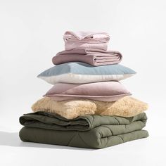 a stack of blankets and pillows sitting on top of each other in different color combinations