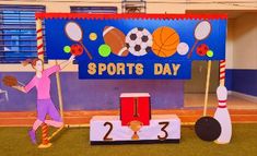 a woman is standing in front of a sports day sign with her arms up and two bowling pins