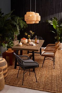 an outdoor dining area with rattan chairs and wooden table surrounded by potted plants