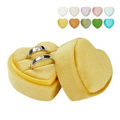 two wedding rings sitting in a heart shaped box with colored hearts around the ring holder