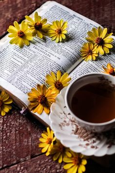 an open book with yellow flowers on it next to a cup of tea