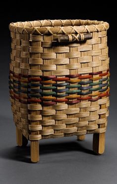 a woven basket sitting on top of a wooden stand in front of a black background