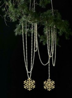 two snowflakes hanging from a tree branch with beads attached to the chains