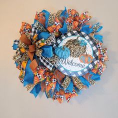 a welcome fall wreath hanging on the wall with blue and orange ribbon, leopard print pumpkins and cheetah