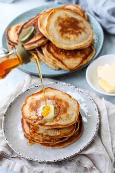 pancakes with syrup being poured onto them and butter on the side, along with honey