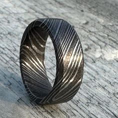 a black ring with an intricate design on it sitting on a wooden surface in the sun