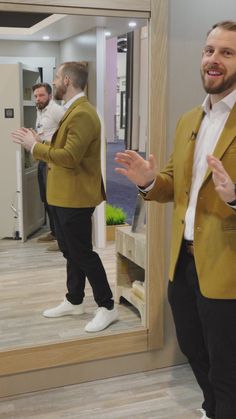 a man standing in front of a mirror wearing a yellow jacket and white shirt with his hands out