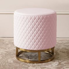 a pink ottoman sitting on top of a rug next to a white and gold stool