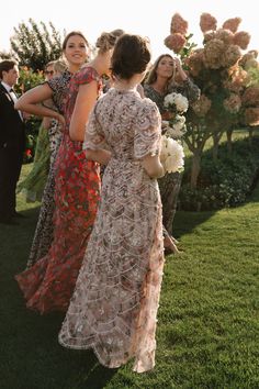 two women standing next to each other on top of a lush green field with flowers