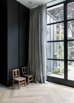 two wooden chairs sitting next to each other in front of a window with curtains on it