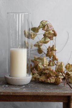 a candle sitting on top of a wooden table next to a vase filled with leaves