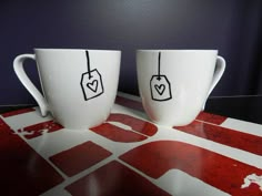 two coffee mugs with tags on them sitting next to each other in front of a wall