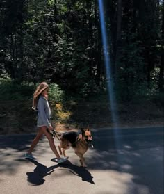 a woman walking her dog on a leash down the street with trees in the background