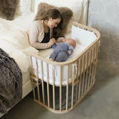 a woman sitting next to a baby in a crib on top of a bed