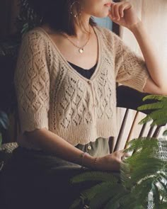 a woman sitting in a chair next to a plant and looking out the window with her hand on her chin