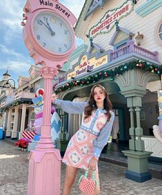 a woman standing next to a pink clock in front of a building with decorations on it