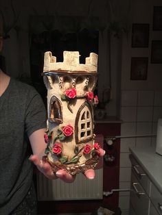 a woman holding up a cake shaped like a house with roses on the front and side