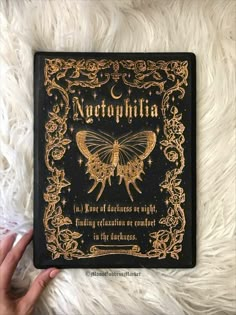 a hand holding a black and gold book on top of a white furnishing