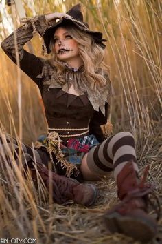 a woman dressed as a scarecrow sitting in tall grass