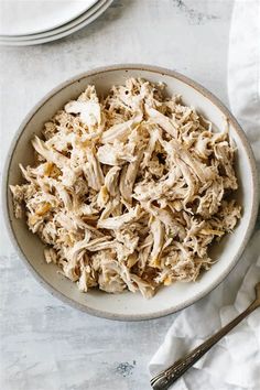 a white bowl filled with shredded chicken on top of a table next to silverware