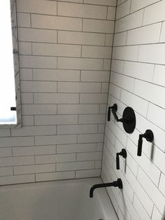 a white tiled bathroom with black faucet and bathtub in the shower area