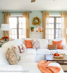 a living room filled with white furniture and lots of orange pillows on top of it