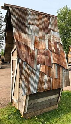 an old rusty tin roof on a wooden shed in the grass with trees and buildings behind it