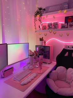 a desk with two computer monitors and a keyboard on it, in front of a pink wall