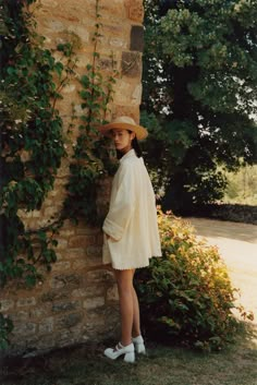 a woman standing next to a brick wall with ivy growing up it's side