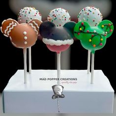 four mickey mouse cake pops on top of a white display stand with colorful toppings