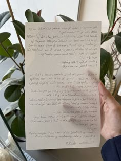 a person holding up a piece of paper with writing on it in front of a potted plant