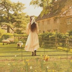 a woman in a white dress is looking at sheep behind a fenced in area