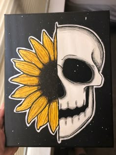 a person holding up a piece of art with a skull and sunflower on it