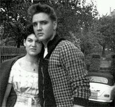 a man and woman standing next to each other in front of a car on the street