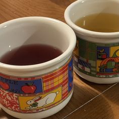 two mugs filled with liquid sitting on top of a wooden table next to each other