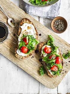 two open faced sandwiches with lettuce, tomatoes and cheese on them sitting on a cutting board